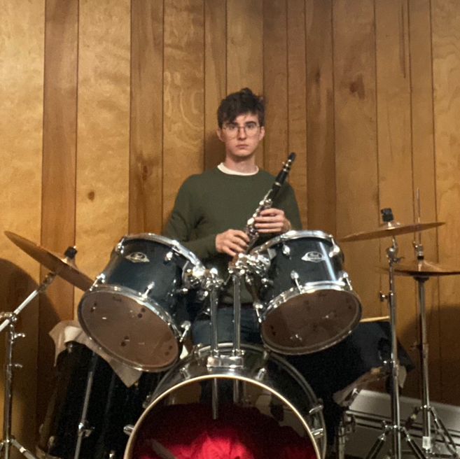 James sitting at a drum set holding a clarinet. He plays neither